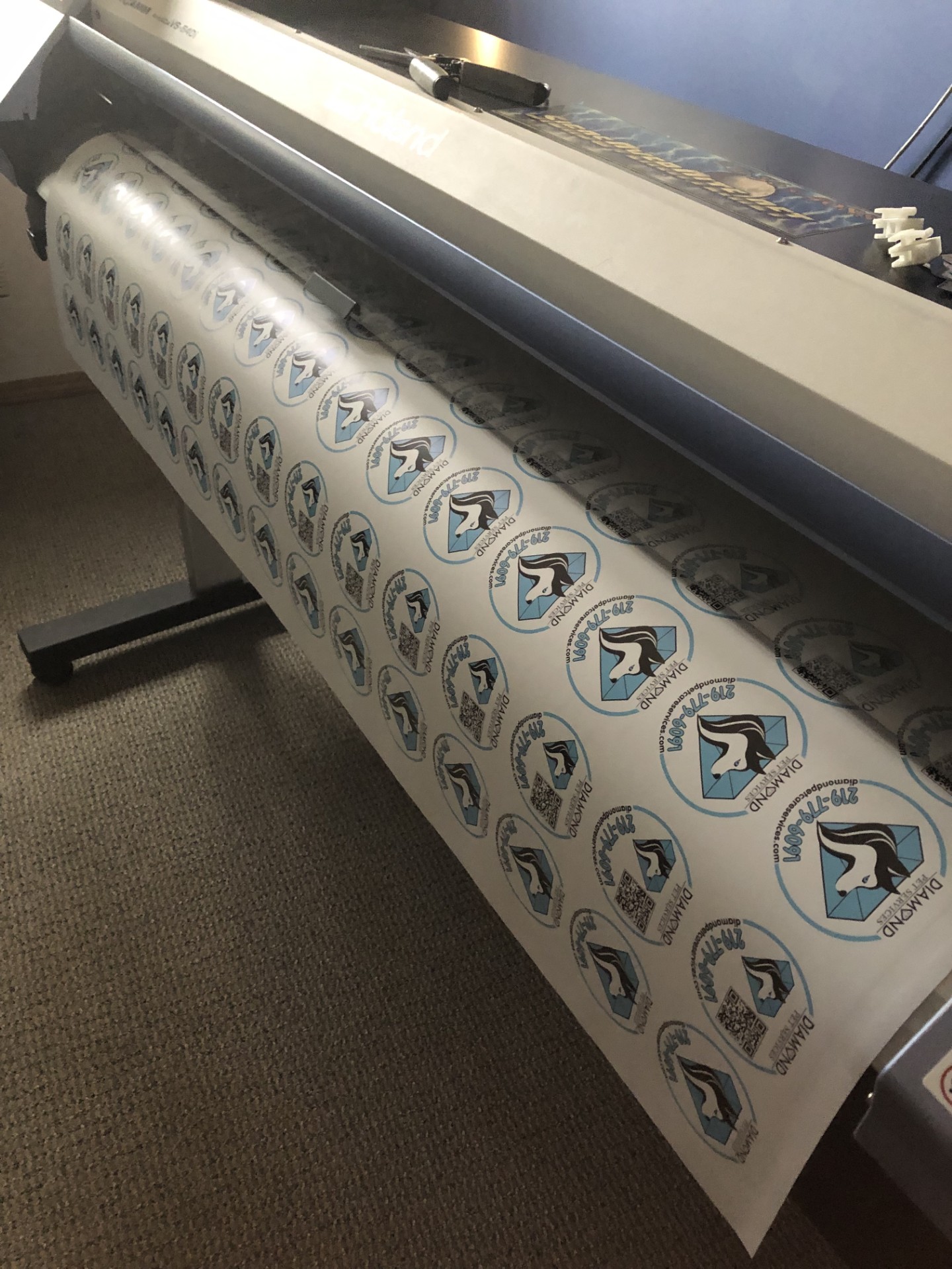 Roll of custom printed round die cut stickers coming off a wide-format printer